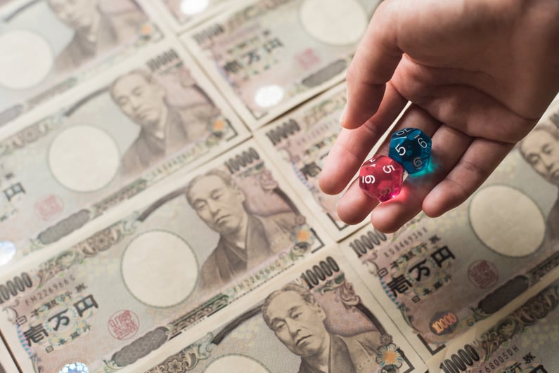 Hand holding dice against background of Japanese currency