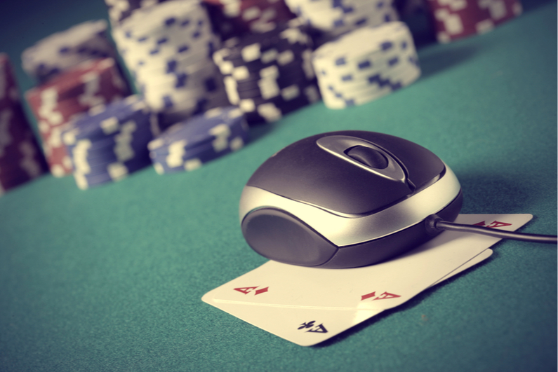 Computer mouse sitting on top of pocket Aces with poker chips in background