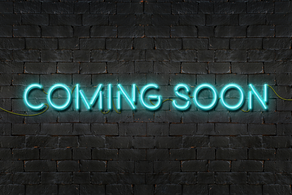 blue neon sign against a brick-wall background reads "coming soon"