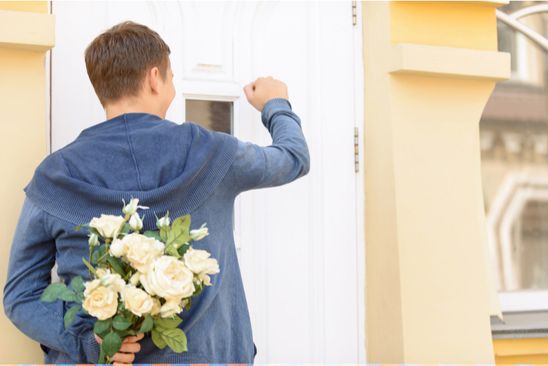 Young man with bouquet of flowers knocking on door